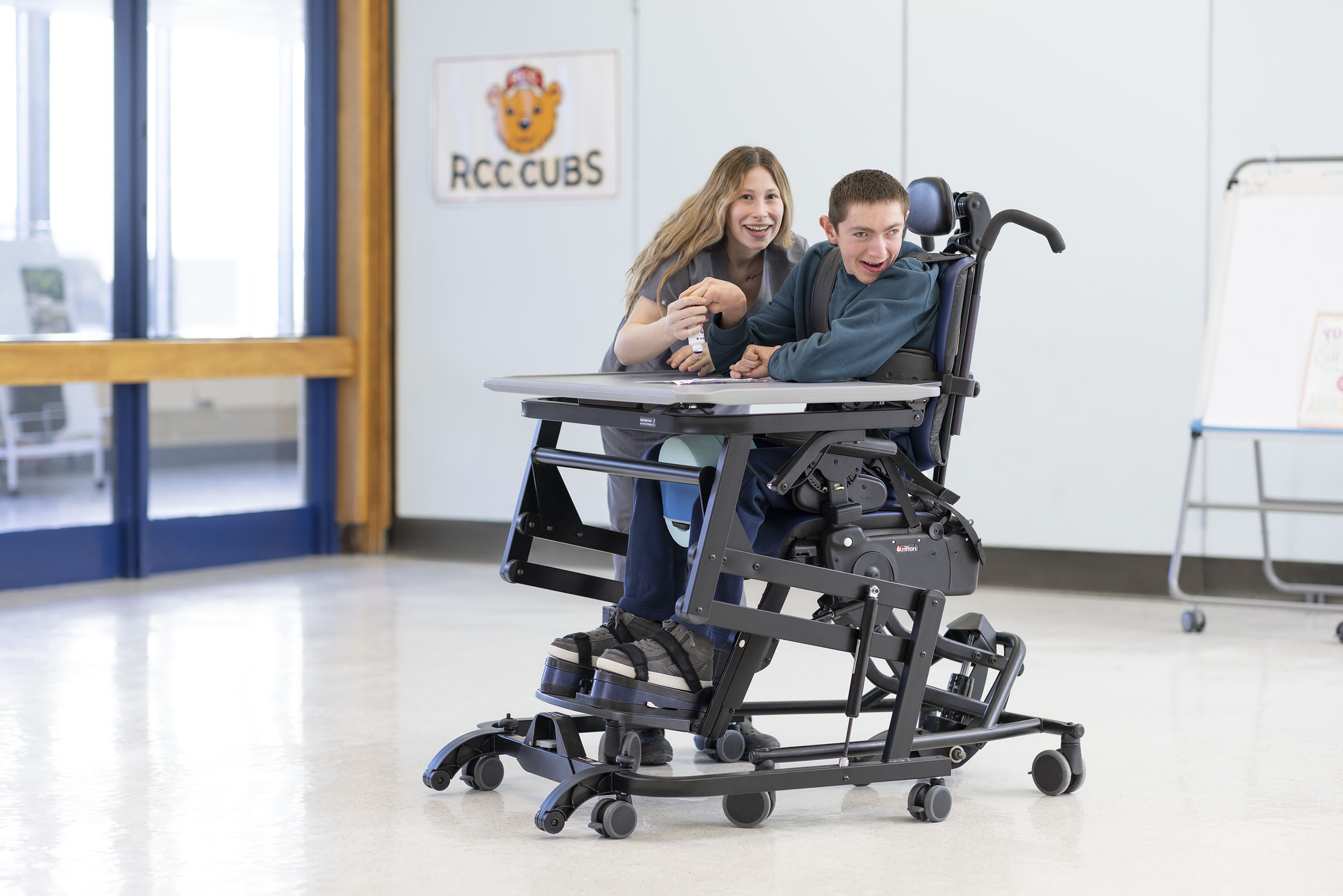 A young man sits in a Rifton Activity Chair at a Rifton Adaptive Desk.