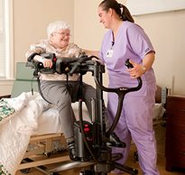 A caregiver using the Rifton TRAM to help an elderly homecare client make a seated transfer into bed.