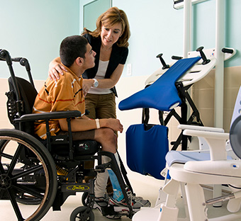 A young man with disabilities transfers out of his wheelchair into a standing position in a Rifton Support Station.