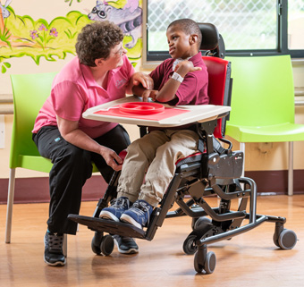 A young man sits in a Rifton Activity Chair and smiles at his caregiver.