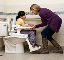 A therapist positions a child with physical disabilities on the toilet using adaptive toileting supports.