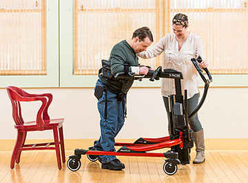 A caregiver helps a young man walk in a Rifton E-Pacer.