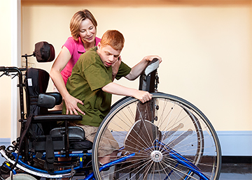 Caretaker helps boy into a wide deck Rifton Mobile Stander