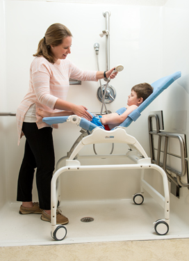A young woman assists a boy in a Rifton Wave bath chair.