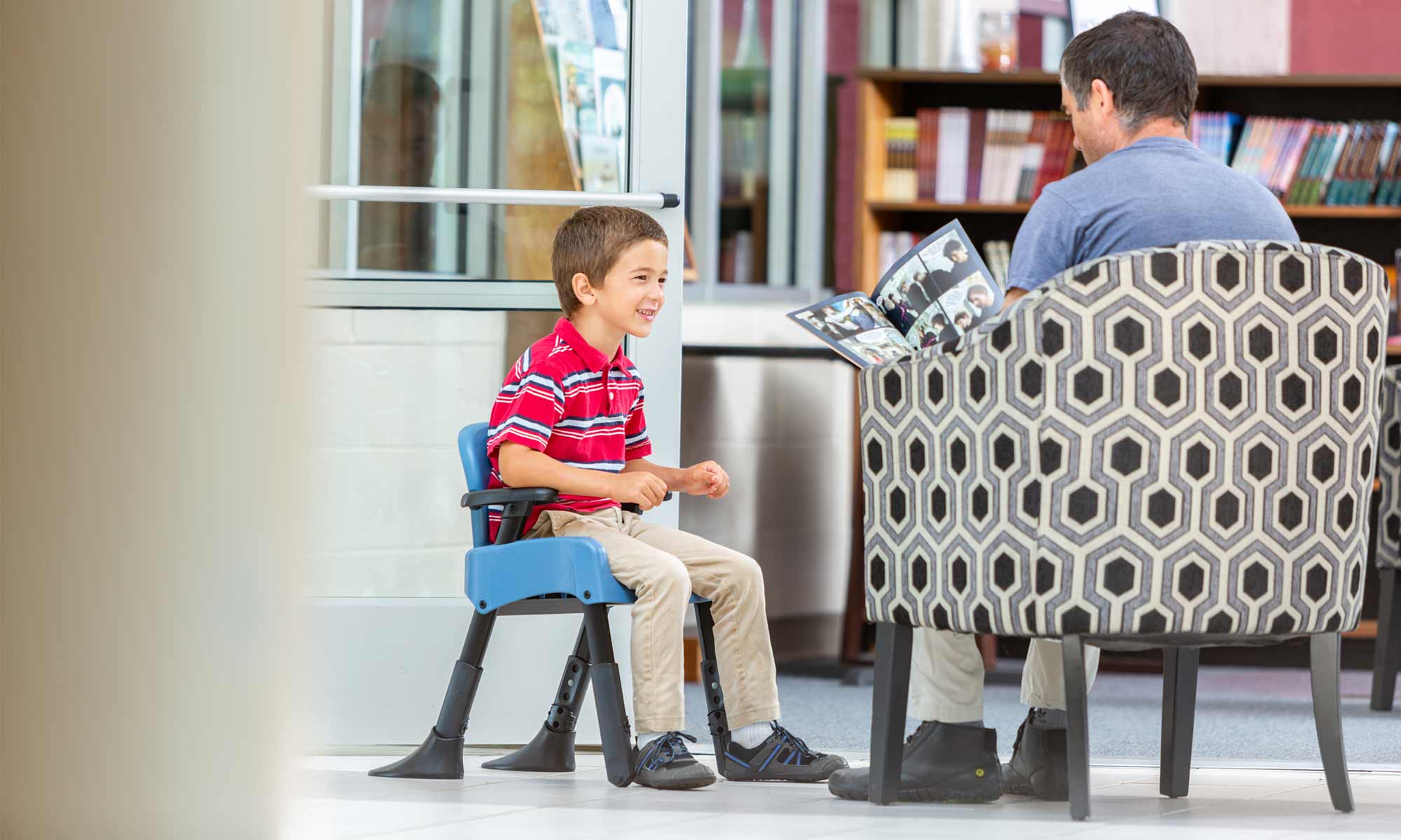 A boy sits in a Rifton Compass Chair and talks with his father.