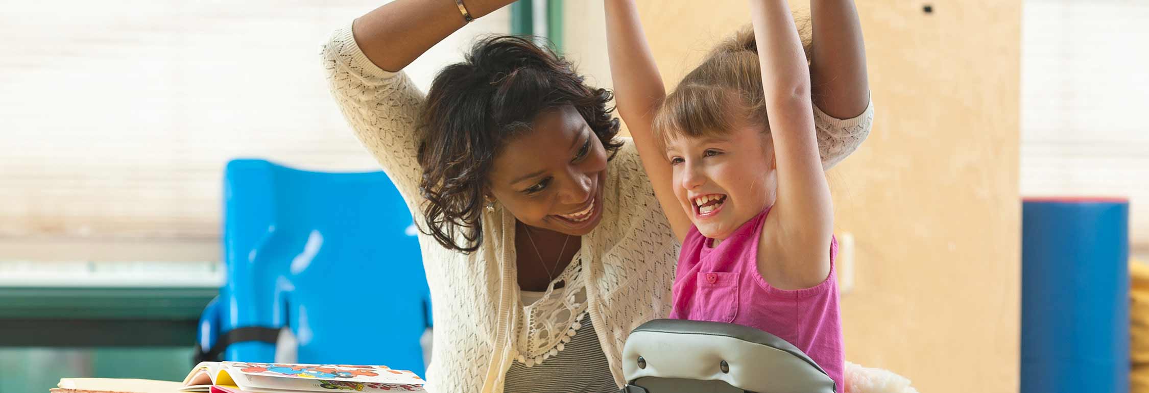 A girl stands in a Rifton Mobile Stander and smiles at her caretaker.