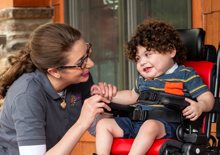 A boy sits in a Rifton Activity Chair and smiles at his caretaker.