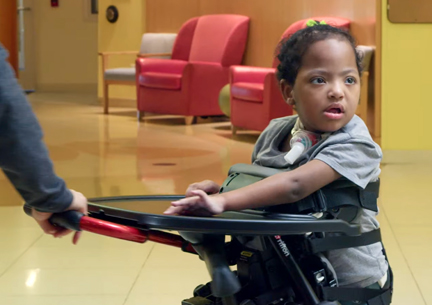 A young girl stands in a Rifton Stander.