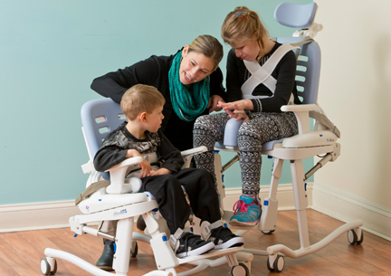 2 children sitting on Rifton HTS chairs, talking with their caretaker.