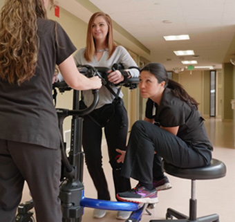 A woman using the Rifton E-Pacer with the assistance of two therapists
