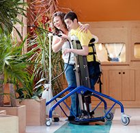 A caregiver waters a a plant with a client who is standing in a Rifton Mobile Stander.