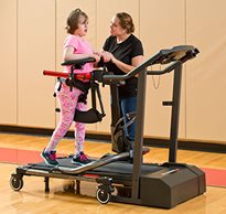 A caregiver encourages a young client with walking excercises on a treadmill using a Rifton Pacer.